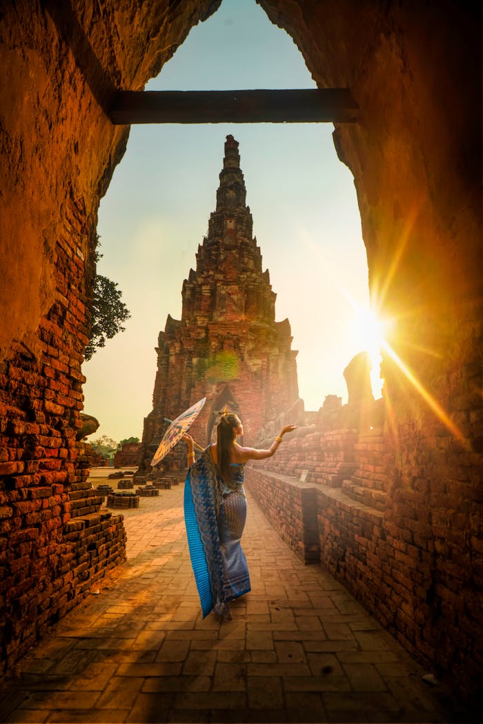 Services A woman in traditional wear stands with an umbrella at a historic Ayutthaya temple during sunset.
